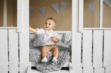 Beyaz tişörtlü, bej şortlu, gülümseyen ve yan bakan genç bir çocuk.