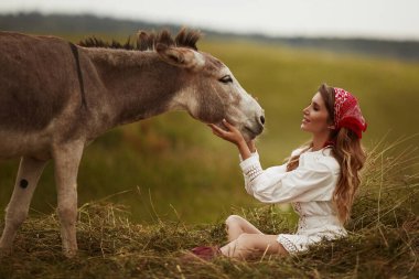 Beyaz cüppeli genç model kadın çayırda sevimli bir eşekle poz veriyor.