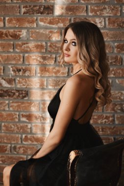 Tuğla duvara karşı siyah elbise giyen, gece makyajlı model bir kızın yan görüntüsü.