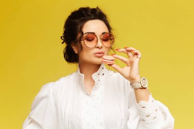 Beyaz elbise giyen, badem kurabiyesi yiyen, sarı arka planda izole edilmiş, fotokopi çekilen bir stüdyo kızı.