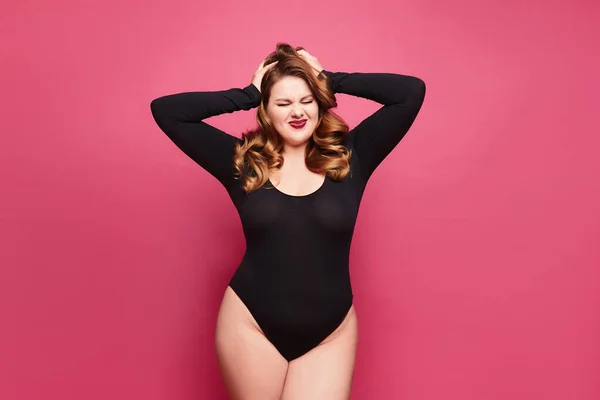 Linda emocional plus-size modelo feminino em um bodysuit preto posando em fundo rosa em estúdio — Fotografia de Stock