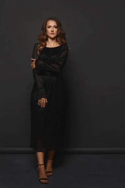 一个穿着黑色晚礼服的模特儿站在黑色背景上 — 图库照片