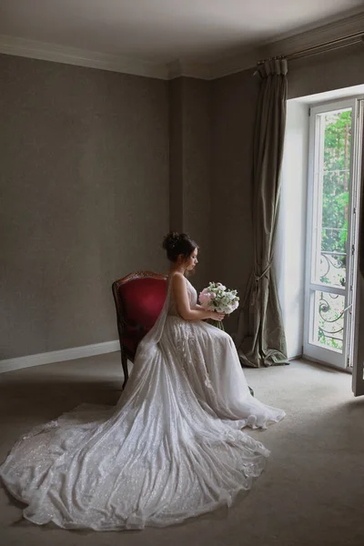 Una hermosa chica modelo en un vestido de novia largo de lujo se sienta en la silla en el interior de la vendimia — Foto de Stock