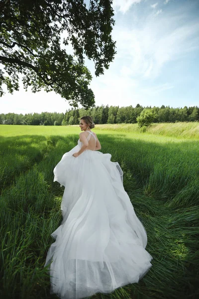 Jovem noiva linda em um vestido de casamento luxuoso correndo fora da cerimônia de casamento através do prado no dia de verão — Fotografia de Stock