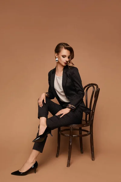 Молода біла жінка в сірому костюмі, блузка і чорне взуття, сидячи на стільці на бежевому фоні, ізольовані з місцем для тексту — стокове фото