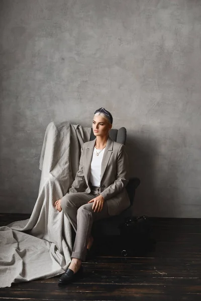 Una giovane donna caucasica con i capelli biondi che guarda da parte mentre è seduta sulla poltrona. Splendida giovane donna d'affari in abito elegante in posa in un interno vuoto — Foto Stock