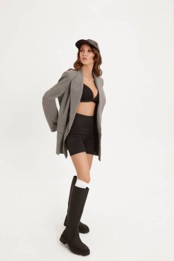 Mükemmel vücutlu yetişkin bir kadın modaya uygun bir ceket giyiyor, şort ve botlar beyaz arka planda poz veriyor, izole edilmiş.