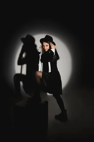 Junge Frau mit schlankem Körper mit schwarzem Hut und kurzem schwarzen Kleid posiert im schwarzen Studio — Stockfoto