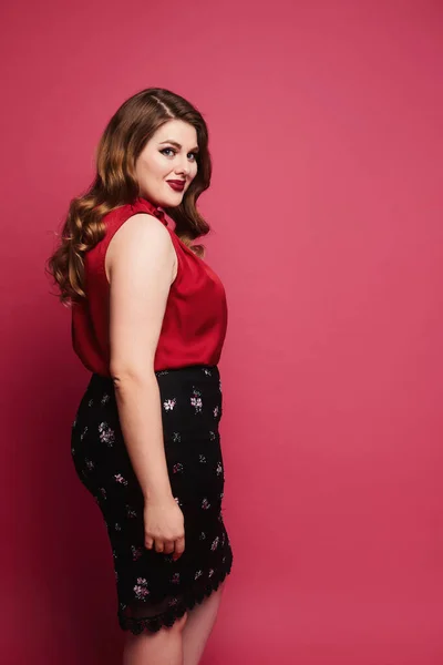 Jovem modelo plus-size menina em blusa de cetim vermelho e saia posando sobre fundo rosa. feliz gordinha mulher no modish roupa sobre rosa fundo — Fotografia de Stock