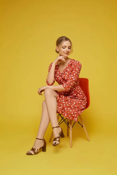 Une fille modèle dans une robe d'été colorée est assise sur la chaise sur fond jaune, isolée. Jeune femme caucasienne dans une robe d'été tendance posant sur un fond jaune. Mode d'été — Photo