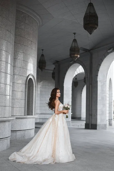 Uma noiva bonita vestindo um luxuoso vestido de noiva rendas posando ao ar livre. Retrato romântico ao ar livre de mulher morena atraente com maquiagem brilhante e penteado de casamento — Fotografia de Stock