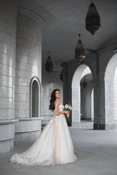 Uma bela noiva jovem vestindo um luxuoso vestido de noiva rendas posando ao ar livre. Retrato romântico ao ar livre de mulher morena atraente com maquiagem brilhante e penteado de casamento — Fotografia de Stock