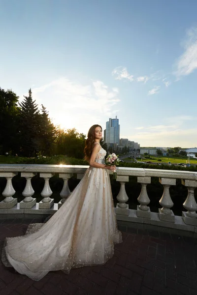 Eine wunderschöne junge Braut in einem luxuriösen Brautkleid aus Spitze posiert im Freien. Romantisches Porträt einer attraktiven brünetten Frau mit hellem Make-up und Hochzeitsfrisur — Stockfoto