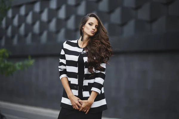 Linda jovem modelo mulher com cabelo escuro perfeito vestindo vestido de noite preto e casaco olhando para câmera posando na cidade. Jovem menina bonita moda em roupa modish — Fotografia de Stock