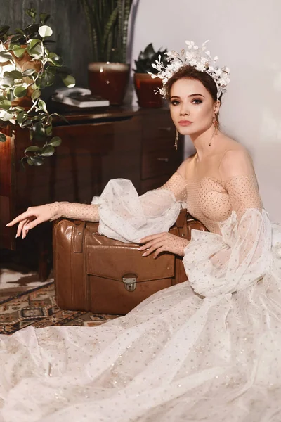 Una novia joven con un elegante peinado de boda con decoración floral que lleva un vestido de novia de moda. Hermosa chica modelo con decoraciones elegantes en su peinado y en un vestido de moda — Foto de Stock