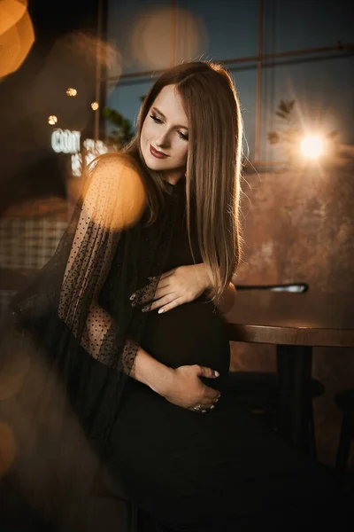 Retrato de close-up na moda de uma jovem grávida com maquiagem brilhante em um vestido preto na moda no interior escuro — Fotografia de Stock
