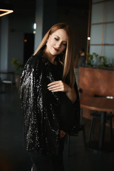 Молода вагітна жінка з яскравим макіяжем в модному чорному платті і модним блискучим піджаком в темному інтер'єрі — стокове фото