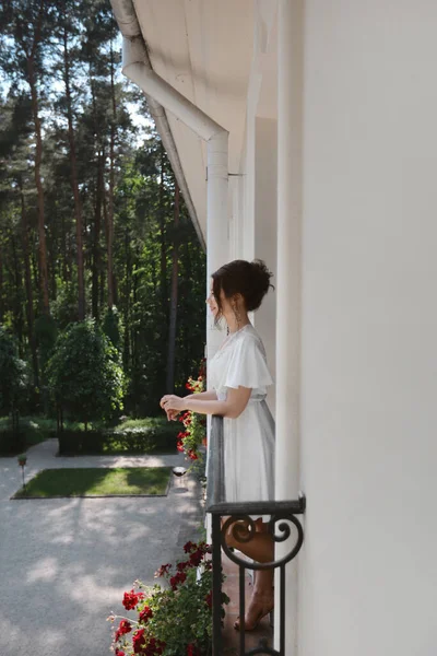 Piękna modelka z ślubnym coiffure w jedwabnym peignir pozuje rano na balkonie. Młoda ładna kobieta, szczęśliwa panna młoda w koronkowym peignir na hotelowym balkonie rano — Zdjęcie stockowe