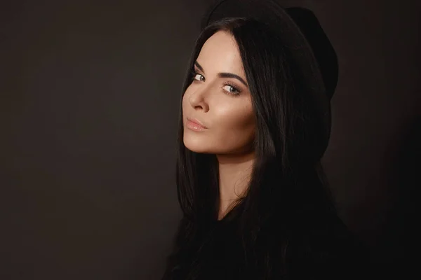 Retrato de moda de uma jovem mulher bonita com maquiagem suave e cabelo preto perfeito em um chapéu preto na moda posando sobre fundo preto — Fotografia de Stock