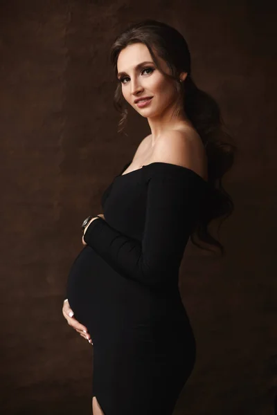 Close-up portret van een prachtige zwangere vrouw het dragen van een zwarte jurk poseren over bruine achtergrond — Stockfoto