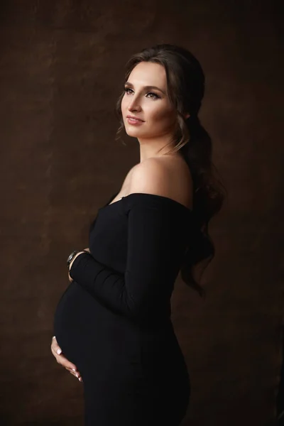 Close-up portret van een prachtige zwangere vrouw het dragen van een zwarte jurk poseren over bruine achtergrond — Stockfoto