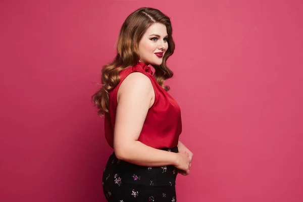 Jovem plus size mulher modelo caucasiano em blusa de cetim vermelho e saia posando sobre fundo rosa. Linda mulher gorda em traje modish sobre fundo rosa — Fotografia de Stock