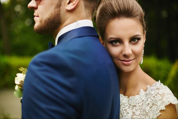 Um casal feliz de recém-casados abraçando e olhando para a câmera. Menina modelo bonita em um vestido de noiva e homem bonito em terno azul na moda — Fotografia de Stock