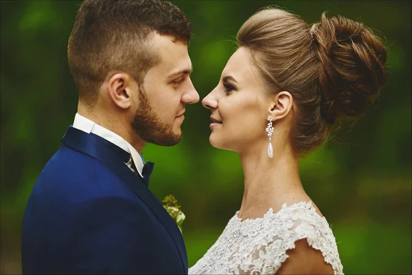 Ein glückliches Brautpaar blickt sich bei der Trauung im Freien in die Augen. Schöne Modell Mädchen in einem Hochzeitskleid und schöner Mann im trendigen blauen Anzug — Stockfoto