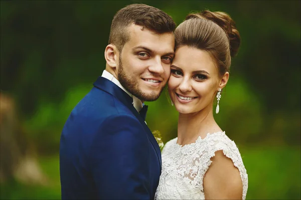 Щаслива пара молодят обіймає і дивиться в камеру. Красива дівчина моделі в весільній сукні і красивий чоловік в модному синьому костюмі — стокове фото