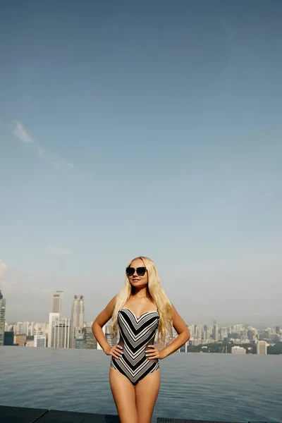 Menina modelo com corpo magro perfeito em um maiô modesto posando na piscina infinita no topo do edifício com uma vista panorâmica de Cingapura — Fotografia de Stock