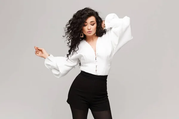 Молода модель жінка з довгим чорним кучерявим волоссям у білій блузці та чорних шортах, позують на білому тлі, ізольовані з місцем для тексту — стокове фото