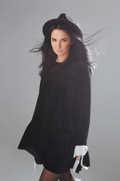 Modell flicka i en kort svart klänning och svart hatt poserar över vit bakgrund i studio. Cosplay av häxa för Halloween — Stockfoto