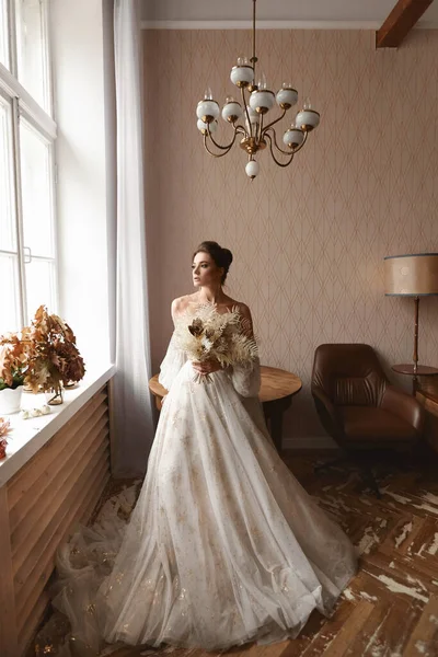 Красивая модель девушка в винтажном свадебном платье с длинными рукавами в помещении. Стильная молодая невеста в модном винтажном платье позирует в интерьере — стоковое фото