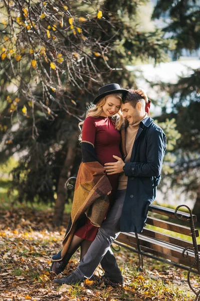Giovane coppia caucasica felice posa all'aperto il giorno d'autunno. Una giovane donna incinta abbraccia il suo uomo e posa al parco della città di autunno — Foto Stock