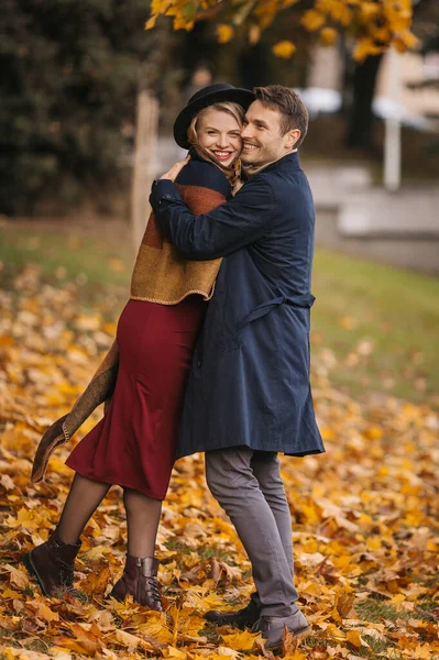 Щаслива гетеросексуальна пара обіймається під час прогулянки в міському парку в осінній день. Красивий чоловік обіймає свою красиву вагітну дружину на відкритому повітрі — стокове фото