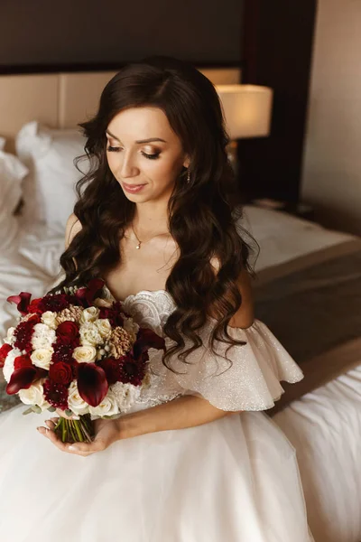 Gorgeous young bride with the bridal bouquet. Bridal fashion model with wedding makeup posing with a wedding bouquet in interior — Stock Photo, Image