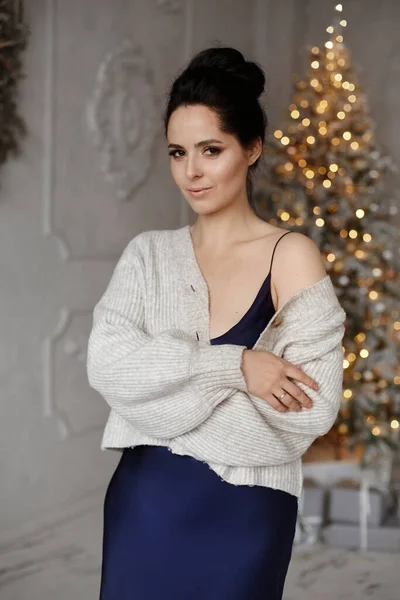 Modieus model meisje met perfecte make-up en kapsel in blauwe jurk en gezellig vest poseren in de voorkant van de kerstboom — Stockfoto