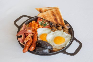 Etli sosis ve mantarlı sahanda yumurta ve beyaz bir tabakta saplı metal bir tabak.