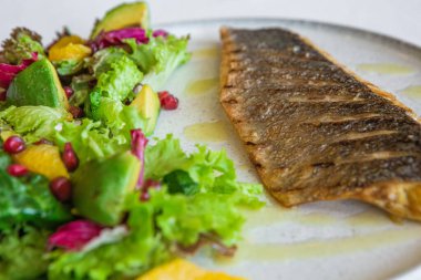 Kızarmış balık, sebze, avokado salatası, ıspanak, portakal ve nar tohumu.