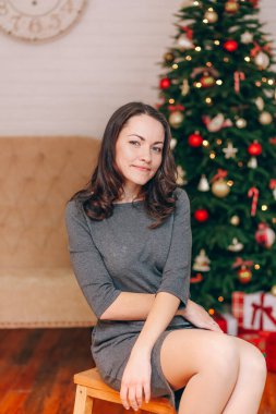 Gülümseyen mutlu bir kadın, dekore edilmiş bir Noel 'in arka planında oturuyor.