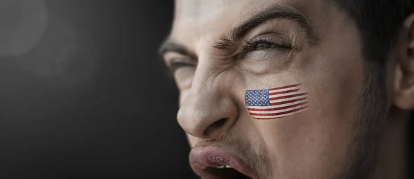 A screaming man with the image of the countrys national flag on his face — Stock Photo, Image