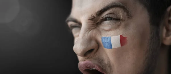 Um homem gritando com a imagem da bandeira nacional da França em seu rosto — Fotografia de Stock