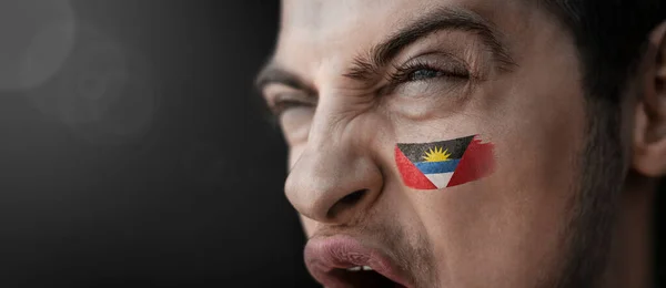 A screaming man with the image of the Antigua and Barbuda national flag on his face — Stock Photo, Image