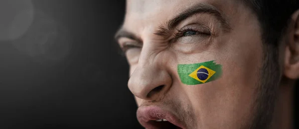 Кричащий человек с изображением национального флага Бразилии на лице — стоковое фото