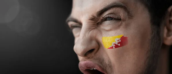 A screaming man with the image of the Bhutan national flag on his face — Stock Photo, Image