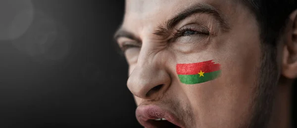 Um homem gritando com a imagem da bandeira nacional do Burkina Faso em seu rosto — Fotografia de Stock