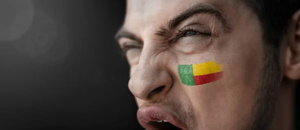 Um homem gritando com a imagem da bandeira nacional do Benim em seu rosto — Fotografia de Stock