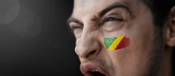 Křičící muž s vyobrazením konžské národní vlajky na tváři — Stock fotografie