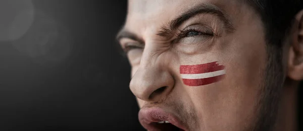 Ένας άντρας που ουρλιάζει με την εικόνα της εθνικής σημαίας της Λετονίας στο πρόσωπό του — Φωτογραφία Αρχείου