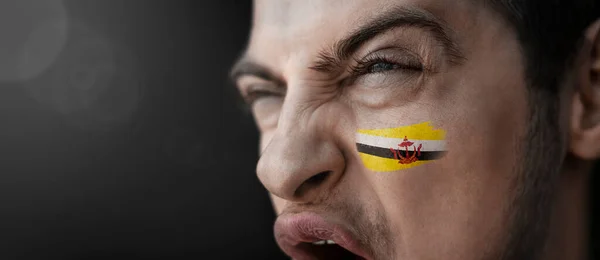 Een schreeuwende man met het beeld van de Brunei nationale vlag op zijn gezicht — Stockfoto